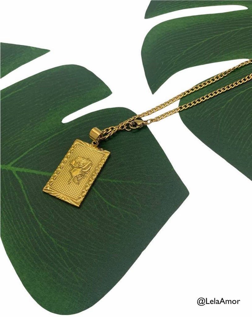 gold rose pendant necklace laying on palm leaf